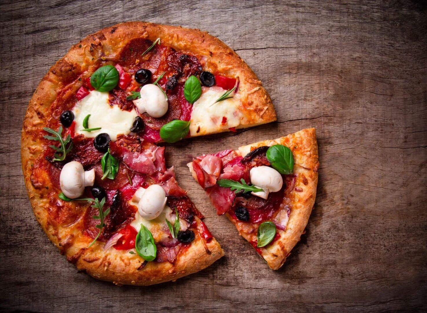 A delicious pizza topped with meat, cheese, and vegetables, placed on a rustic wooden table.