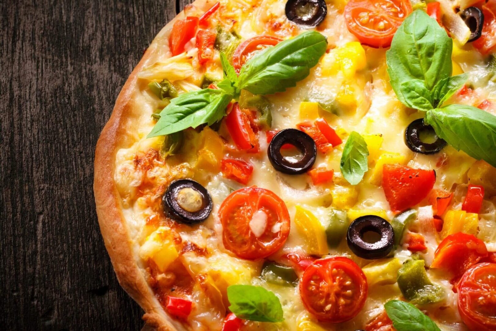 Pizza with fresh tomatoes, olives, peppers, and basil leaves.